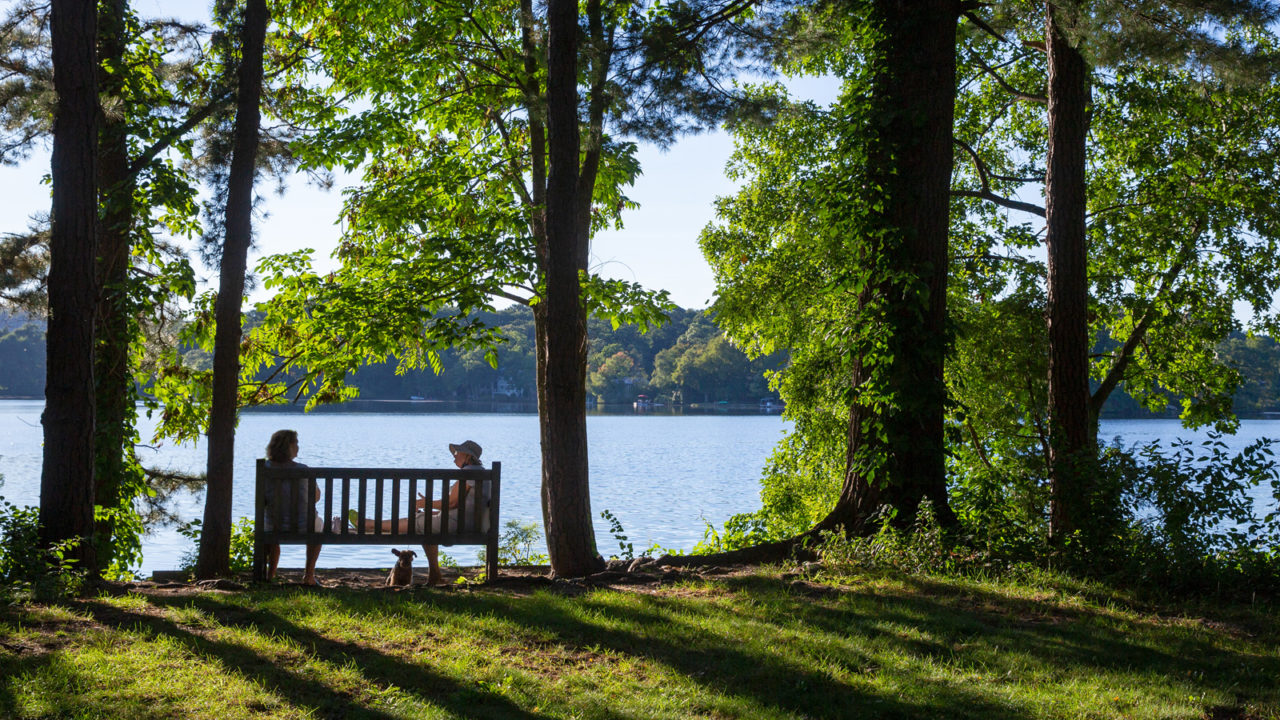 Two women talk on bench overlooking pond