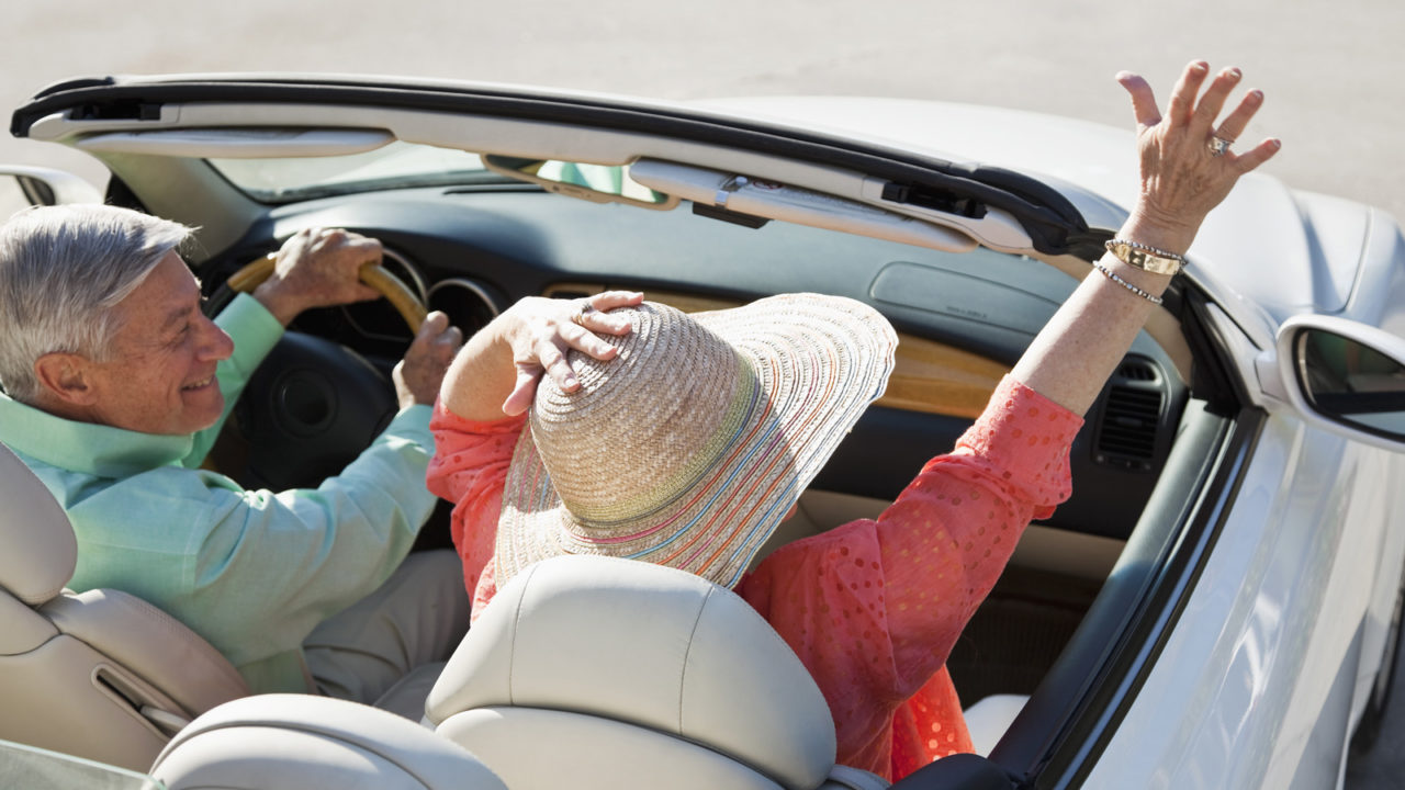 Man in blue shirt, woman in pink waving from convertible