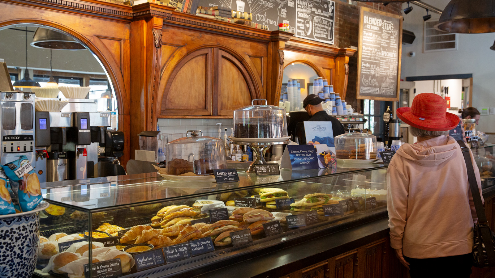 Pastry display case attracts woman in pink hat.