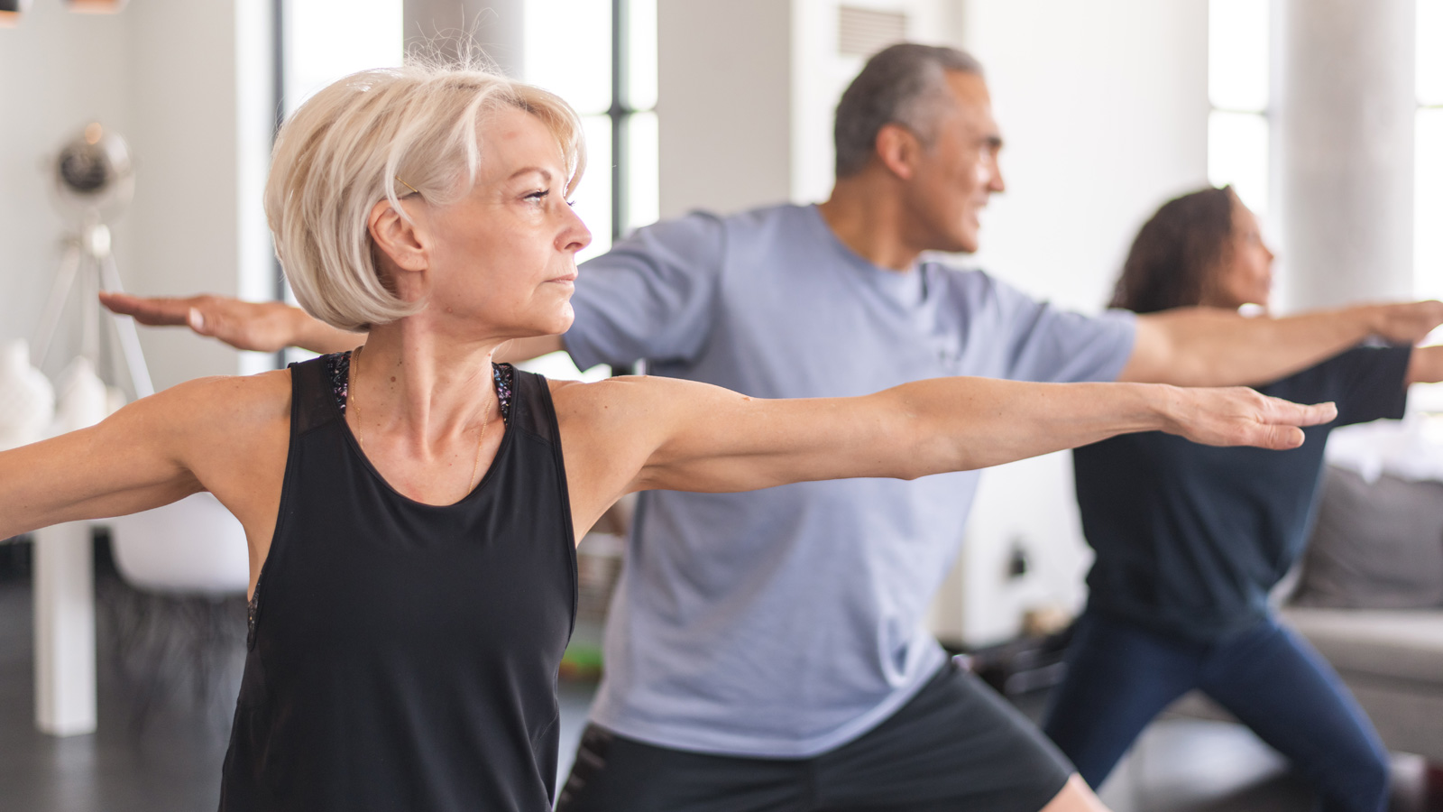 Woman in black tank, man in blue shirt doing yoga pose