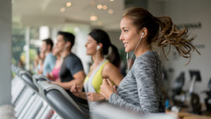 People on treadmills, young woman with bouncing pony tail and earpods in foregrownd