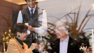 Older Asian couple toasting with waiter hold bottle behind them